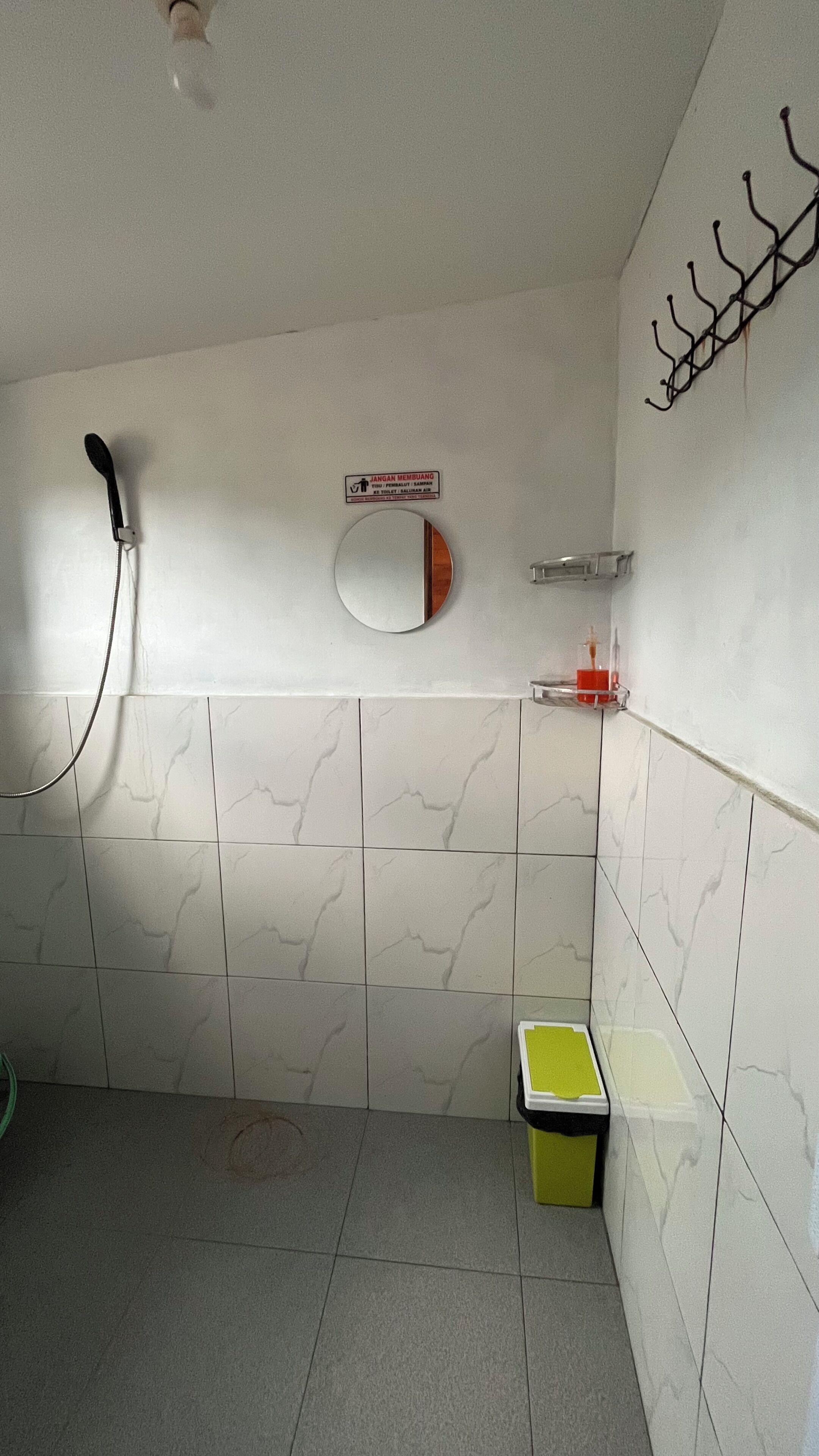 A bathroom with white marble tiles, a shower, a toilet, and a small trash bin.