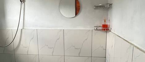 A bathroom with white marble tiles, a shower, a toilet, and a small trash bin.