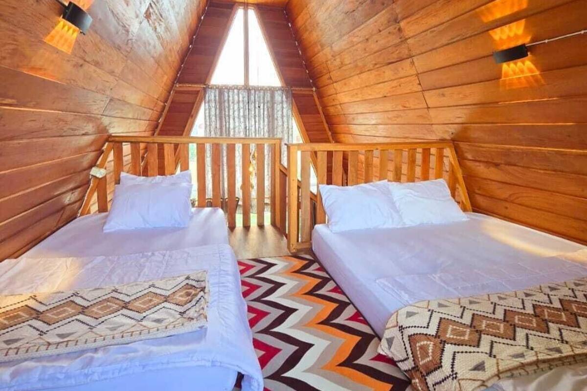 A cozy attic bedroom with two beds, wooden walls, and a view through a window.
