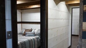 A bedroom with a wooden ceiling, a bed with patterned bedding, and a wooden floor. - The Barn at Reed | Hot Tub + Horse Friendly (Reeds)