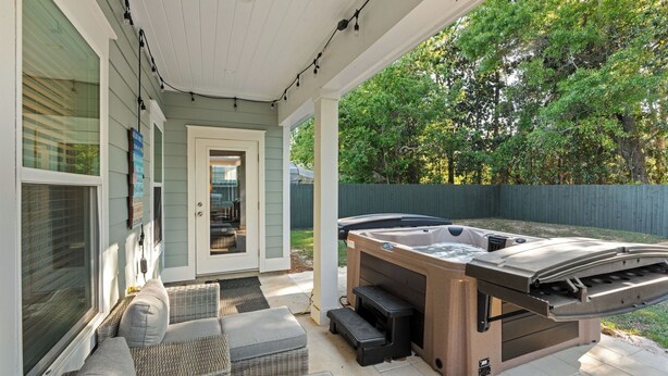 A covered patio with a hot tub, wicker furniture, and a view of the backyard. - Central Pines by Avantstay 30A Wooded Retreat Hot Tub + Private Yard Near Beaches (Santa Rosa Beach)