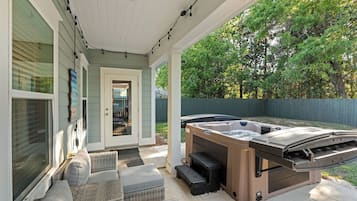 A covered patio with a hot tub, wicker furniture, and a view of the backyard.