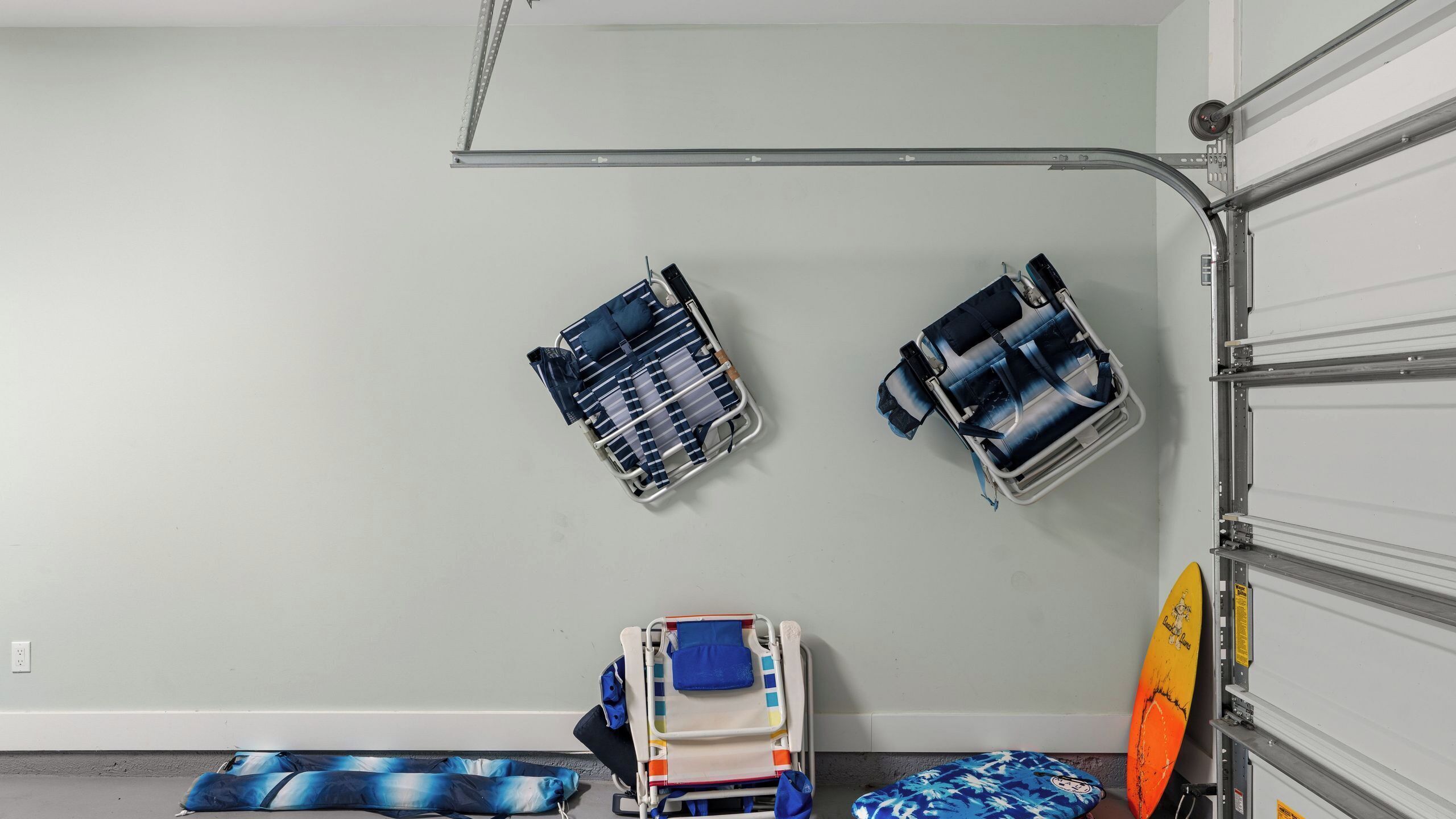 A garage with two wall-mounted storage units, a folding chair, and a surfboard.