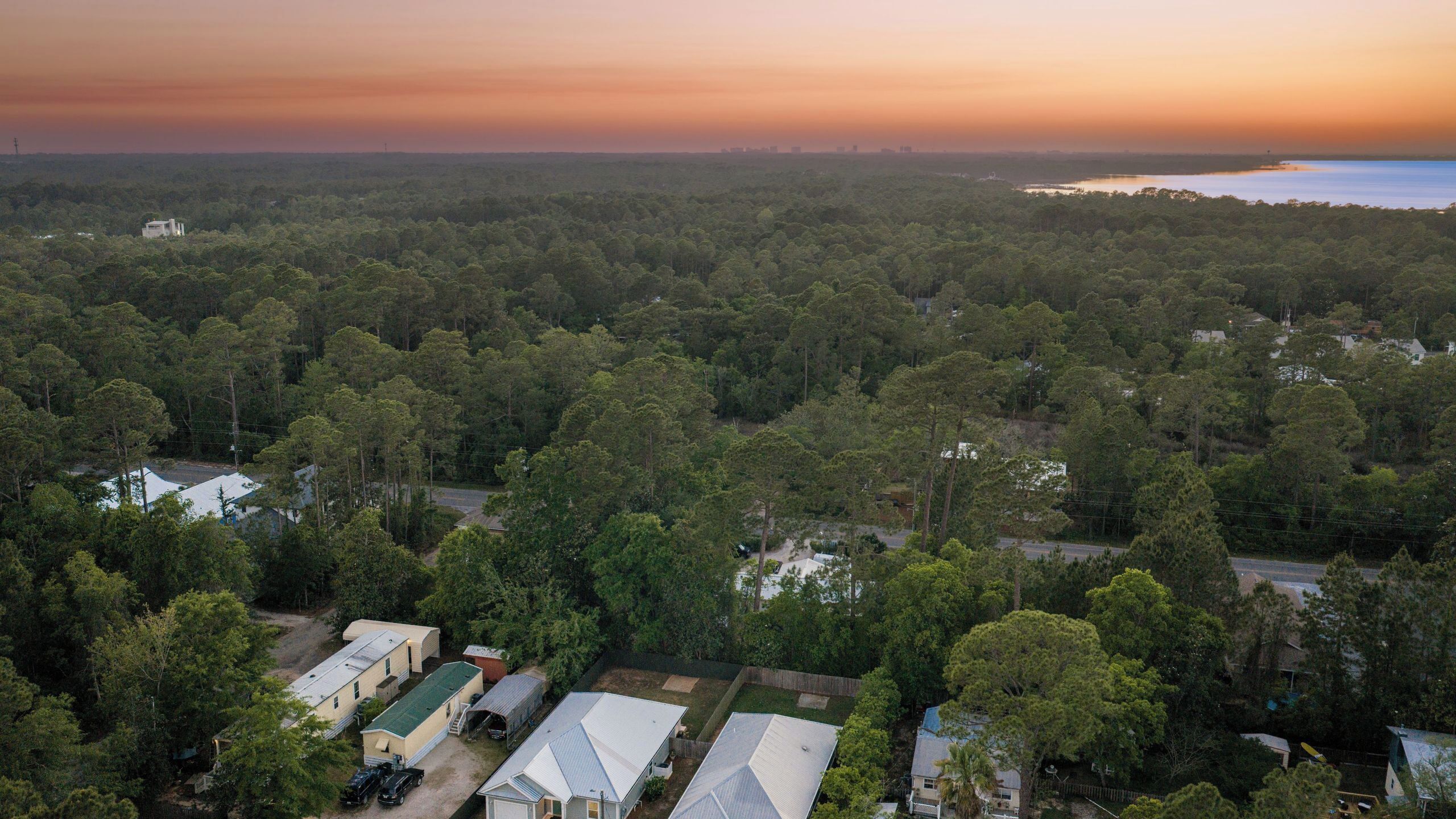 An aerial view of a residential area with houses, a road, and a body of water in the distance.