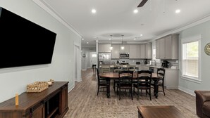 A modern kitchen with grey cabinets, a central island, and a dining area with a round table and chairs. - Central Pines by Avantstay 30A Wooded Retreat Hot Tub + Private Yard Near Beaches (Santa Rosa Beach)