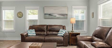 A living room with a brown leather sofa, a wooden coffee table, and a painting on the wall.