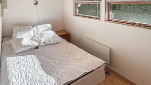 A bedroom with a bed, two windows, a radiator, and a wooden nightstand.