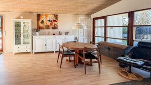 A dining area with a wooden table and chairs, a white cabinet with glass doors, a painting on the wall, and a large window with a view.