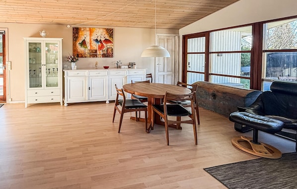 A dining area with a wooden table and chairs, a white cabinet with glass doors, a painting on the wall, and a large window with a view.