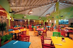 A restaurant with multiple tables and chairs, a high ceiling with exposed beams, and a green wall with a tropical mural. - Cozy 1-bedroom condo with AC in fabulous Oranjestad (Oranjestad)