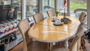 Un comedor con sillas de mimbre, una mesa redonda y vistas a través de amplios ventanales.