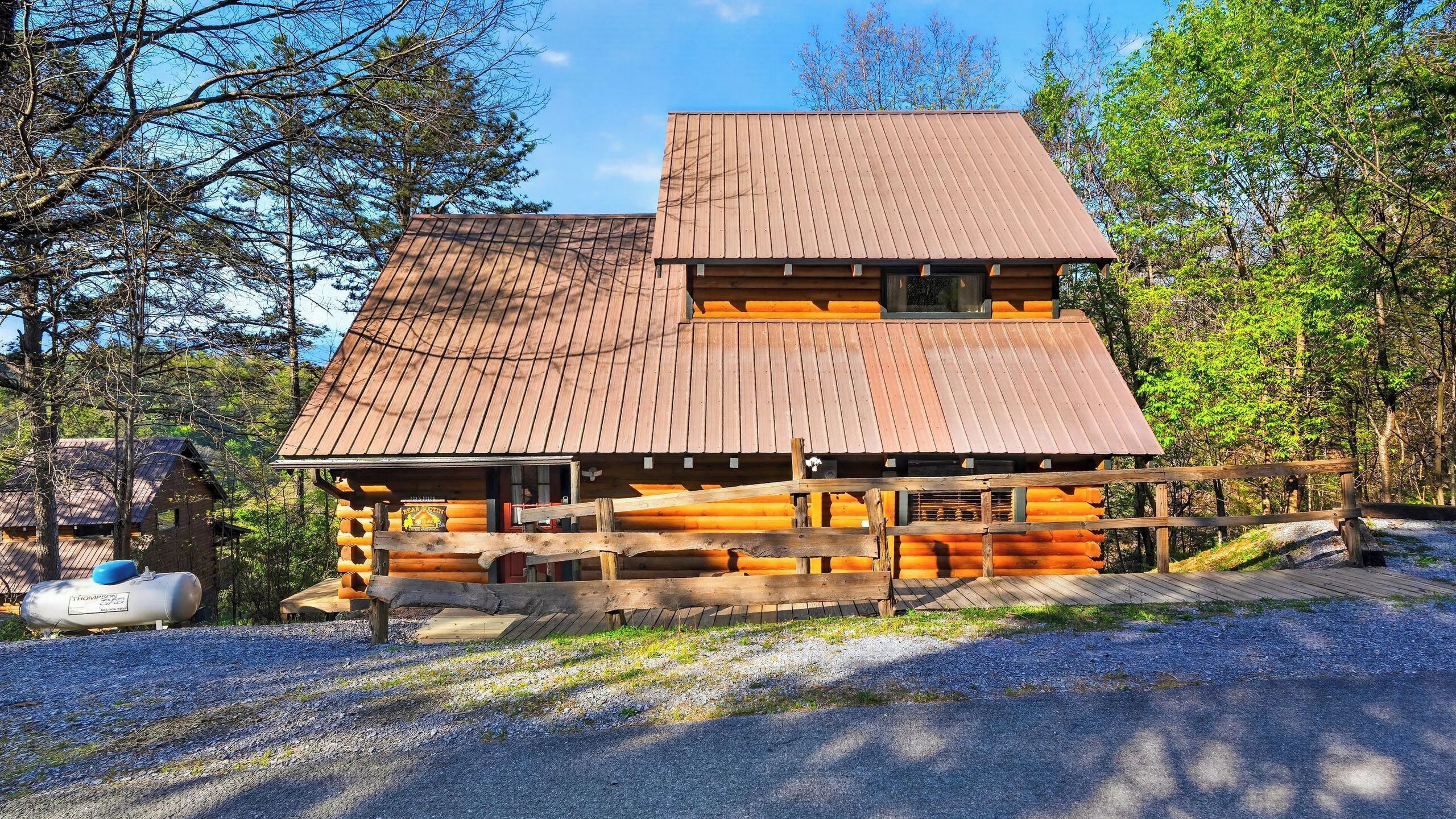 A log cabin with a wooden deck and a metal roof, surrounded by trees.