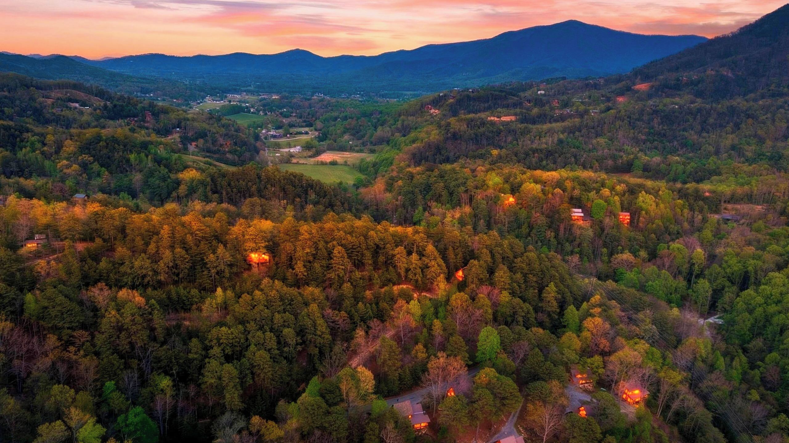 An aerial view of a forested valley with scattered buildings, roads, and a distant town.