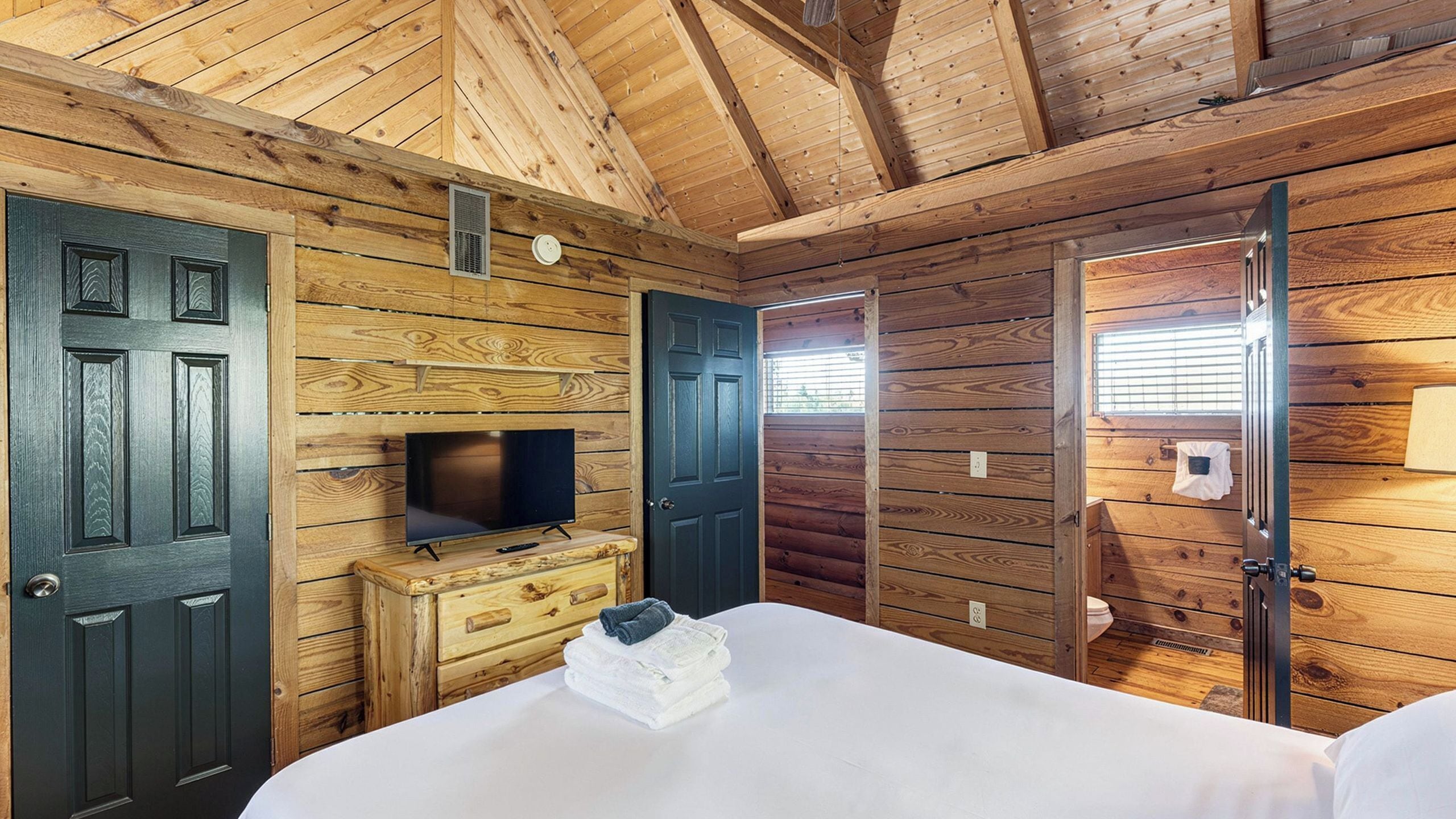 A wooden cabin room with a bed, a TV, and a dresser.