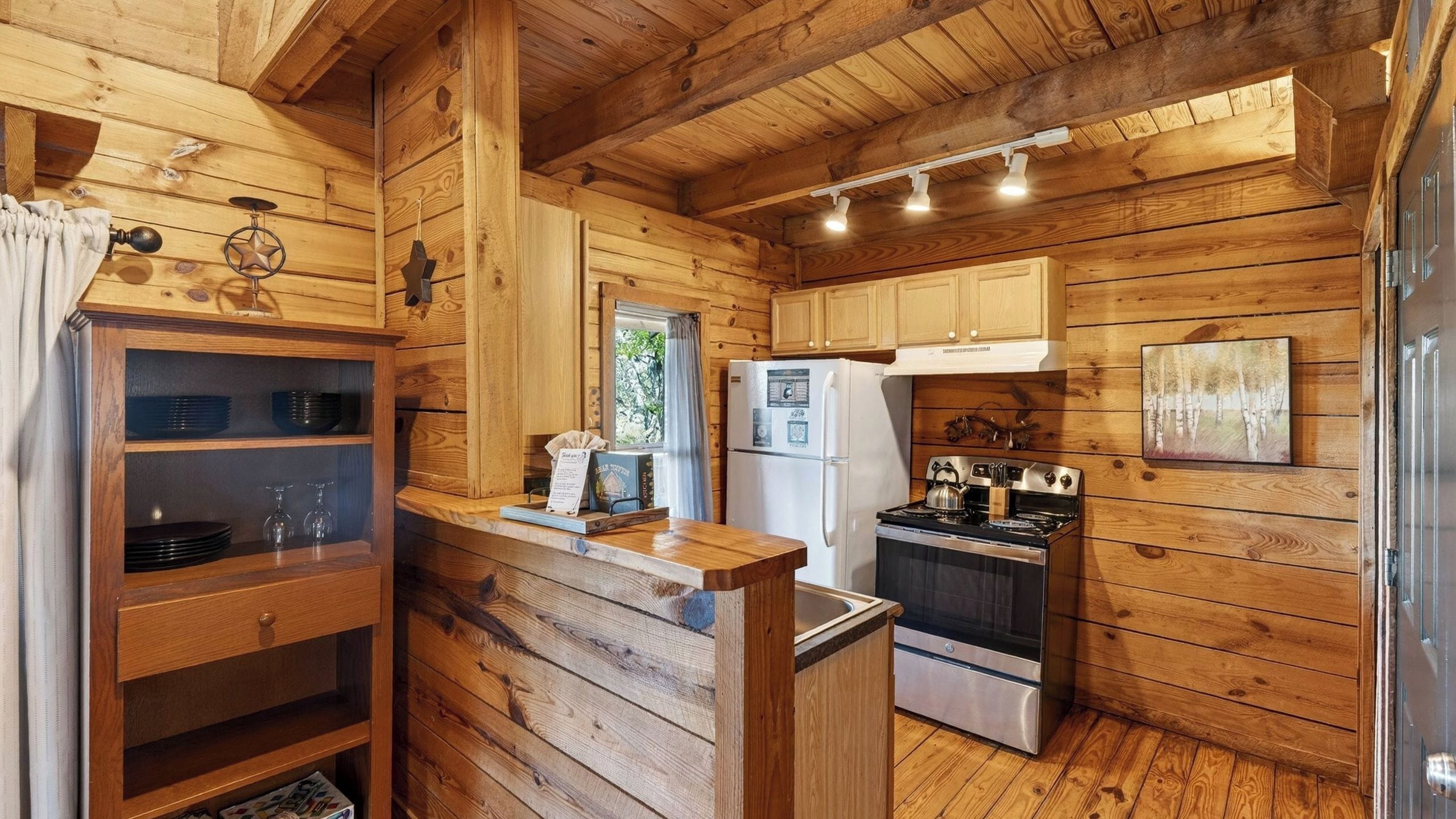 A wooden cabin-style kitchen with a refrigerator, stove, and wooden cabinets.