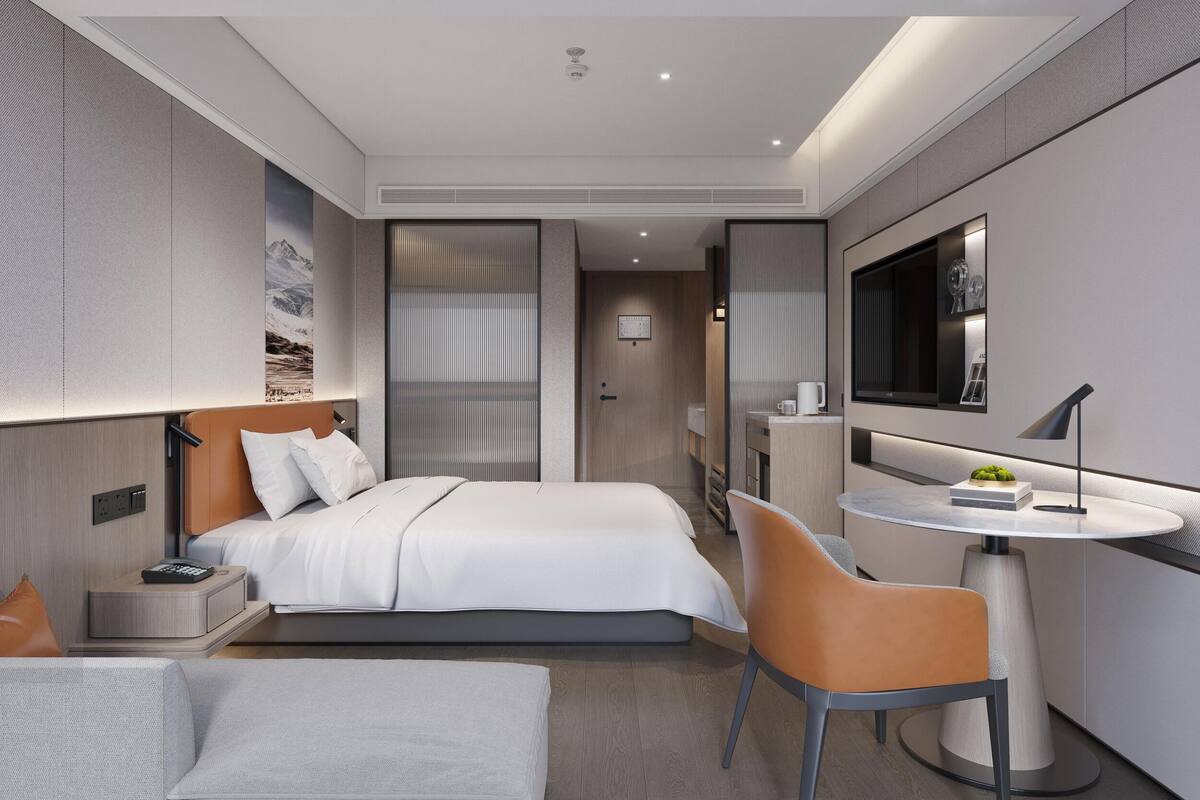 Quarto de hotel moderno com cama, escrivaninha, cadeira, mesinha e televisão.