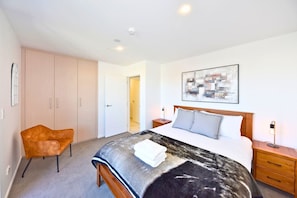 A bedroom with a bed, a chair, a wardrobe, a bedside table, and a wall-mounted artwork. - City Escape in the Heart of Christchurch (Christchurch)