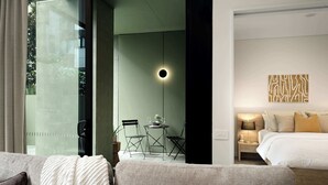 Moderni hotellihuone, jossa on sänky, yöpöytä, lamppu ja lasiovesta avautuva näkym ä ulos.