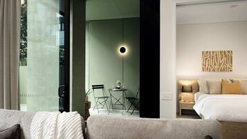 A modern hotel room with a bed, bedside table, lamp, and a view of the outdoors through a glass door.