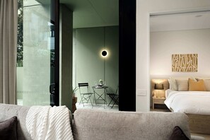 Ein modernes Hotelzimmer mit Bett, Nachttisch, Lampe und Blick ins Freie durch eine Glastür.