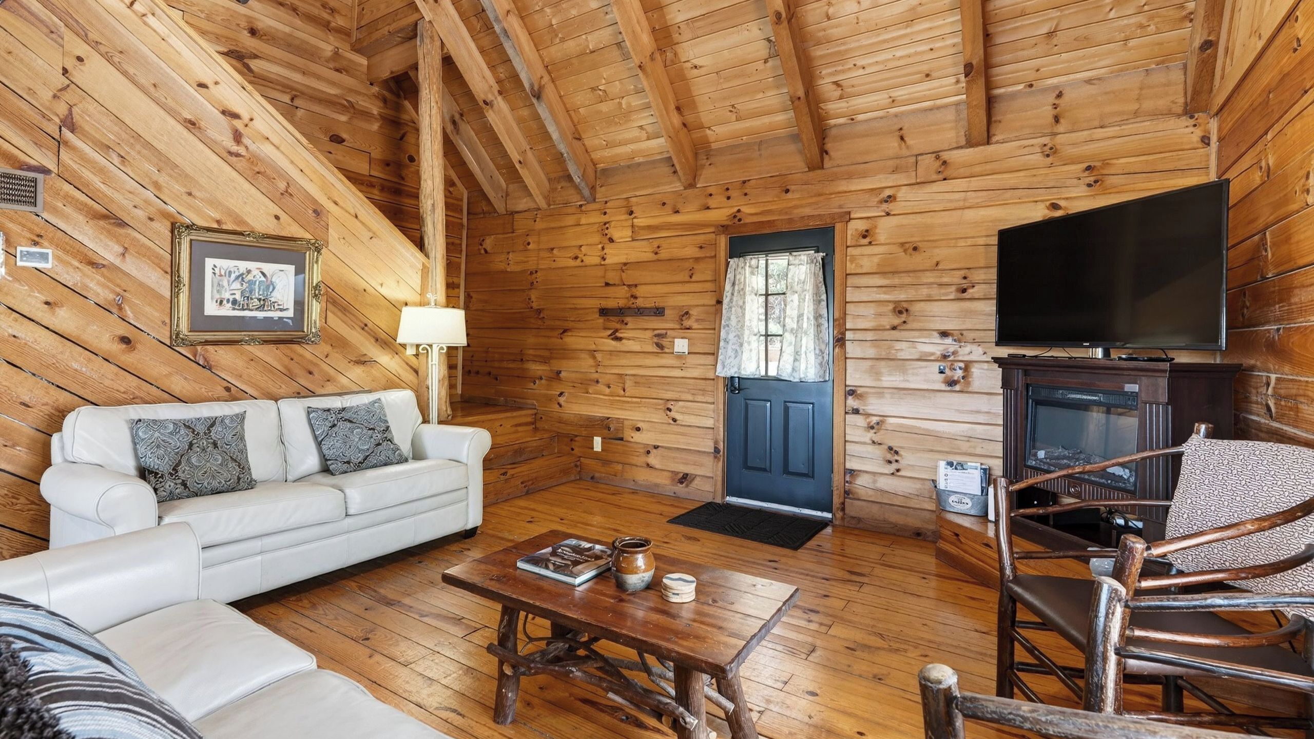 A log cabin interior with a sofa, coffee table, fireplace, and television.