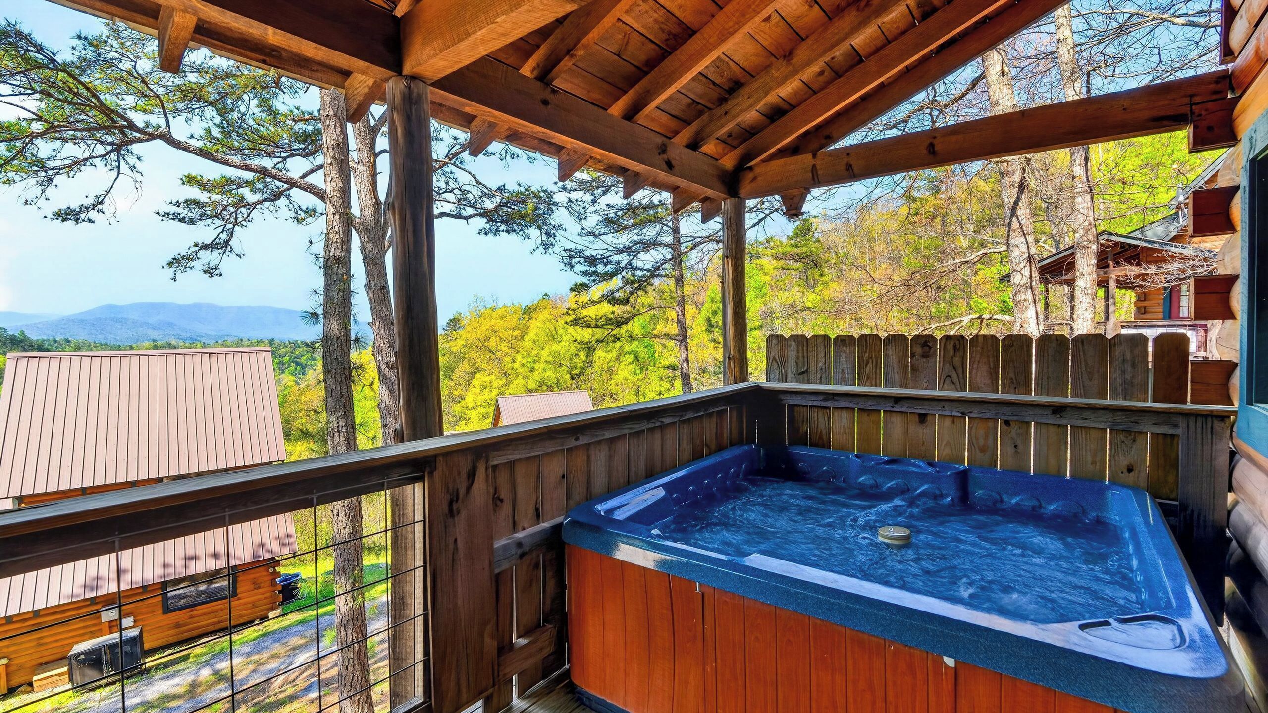 A wooden deck with a hot tub, wooden railings, and a view of trees and mountains.