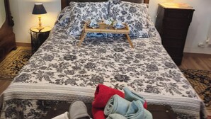 Un lit bien fait, recouvert d’une couvre-lit à motifs floraux, une table de chevet avec une lampe et un tableau accroché au mur.