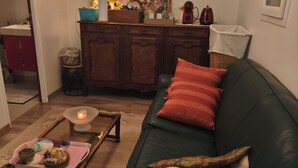 Un salon avec un canapé vert foncé, un meuble en bois, une petite table avec une bougie et des tableaux encadrés accrochés au mur.