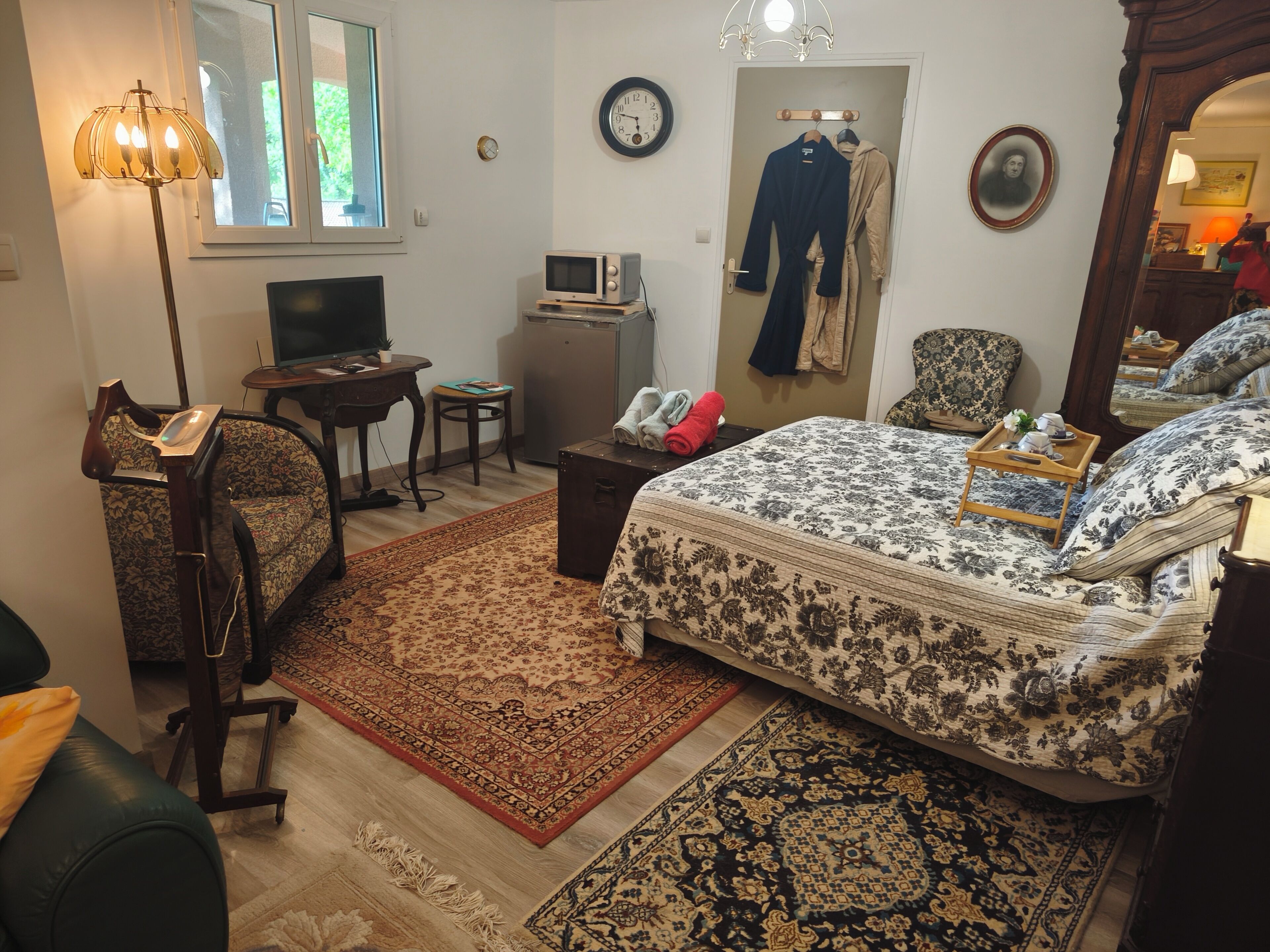 Une chambre à coucher comprenant un lit, un bureau, une chaise, un téléviseur, une horloge et un miroir.