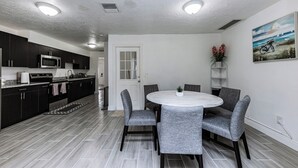 Une cuisine moderne avec des meubles de couleur sombre, un four à micro-ondes et un évier. On y trouve également un coin repas avec une table ronde et des chaises grises.