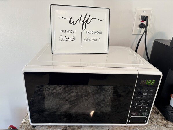 A white microwave oven with a digital display, a control panel with various cooking options, and a sign on top indicating a network password for 'Cabin 3'.