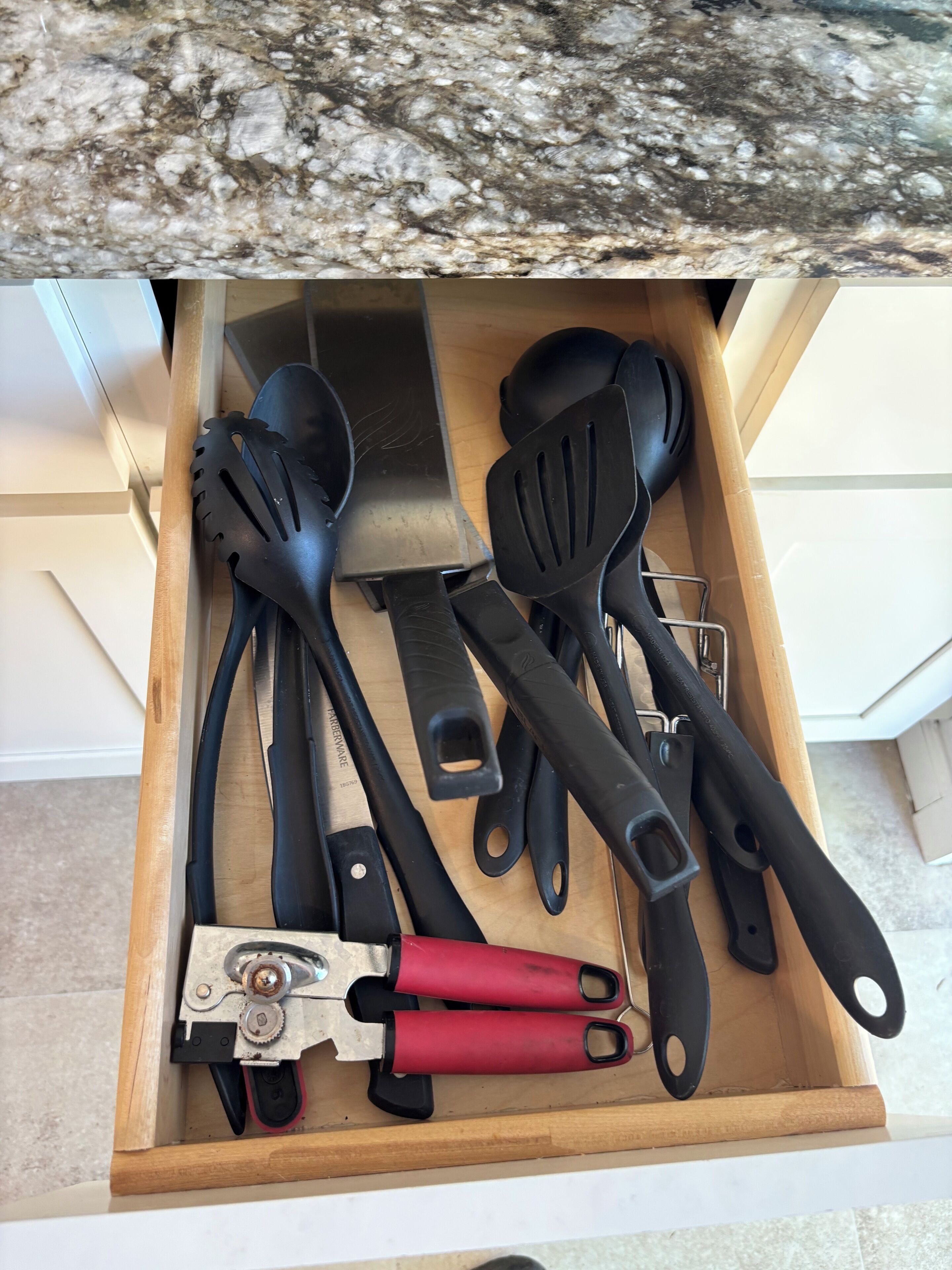 A drawer containing various kitchen utensils including spatulas, a grater, and a pair of scissors.
