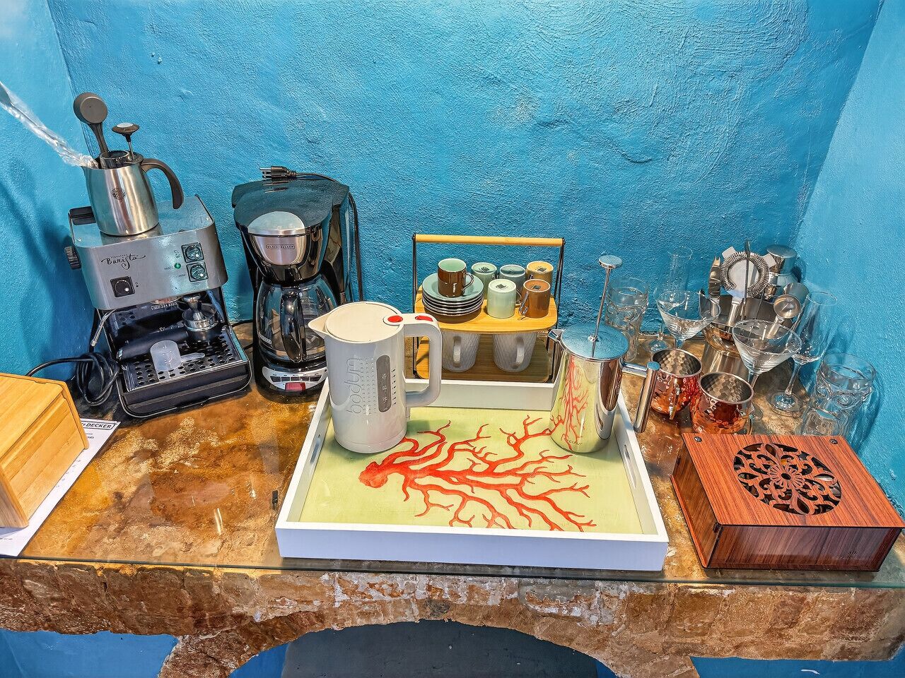 En bordplade med kaffemaskine, elkedel, kaffekande, en bakke med en dekorativ genstand og en trækasse.
