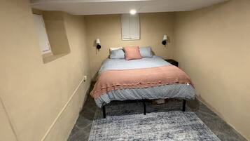 Een slaapkamer met een bed, een vloerkleed, een raam en een wandlamp.