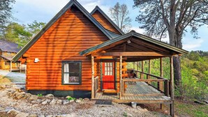 A log cabin with a porch, a red door, and a window.