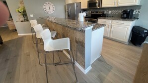 Eine moderne Küche mit weißen Schränken, einer Granit Arbeitsplatte, Edelstahlgeräten und einer Bar mit weißen Hocker.