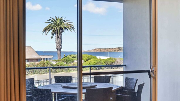 Un balcón con mesa y sillas, una palmera y vistas al mar y las colinas.