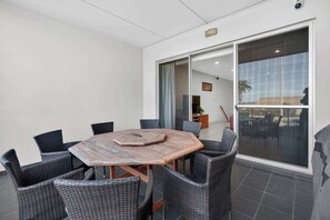 A conference room with a wooden table and wicker chairs, a sliding glass door leading to a balcony, and a view of the outdoors. - No#2 The Block Appartment (Victor Harbor)