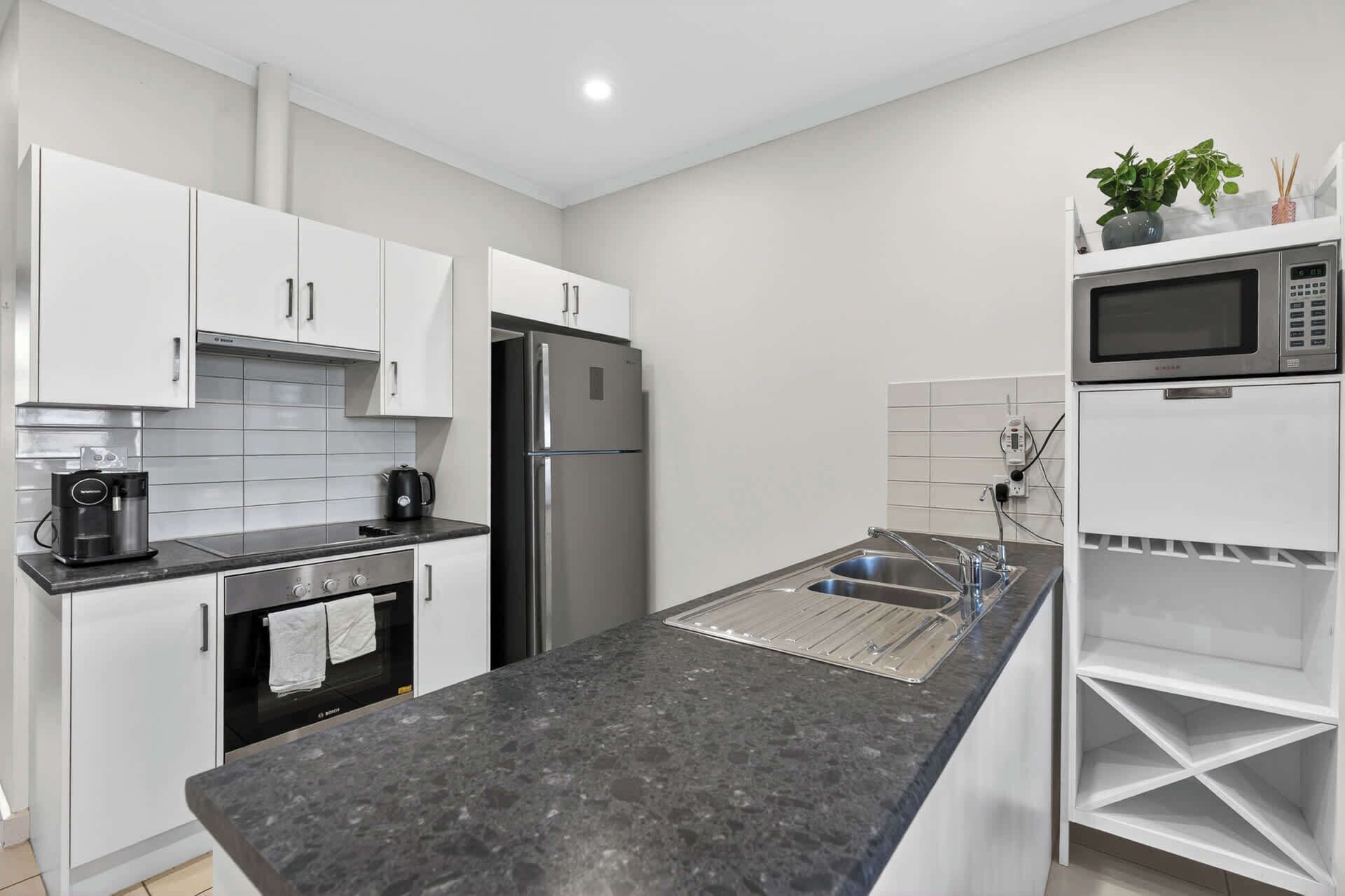 A modern kitchen with white cabinets, a stainless steel refrigerator, a built-in oven, a coffee machine, and a microwave.