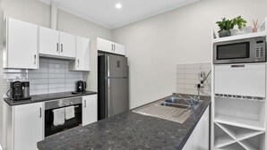 Una cocina moderna con armarios blancos, un refrigerador de acero inoxidable, horno empotrado, cafetera y microondas.