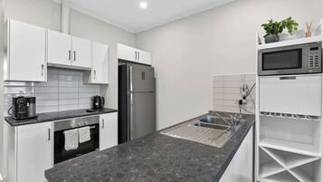 A modern kitchen with white cabinets, a stainless steel refrigerator, a built-in oven, a coffee machine, and a microwave.