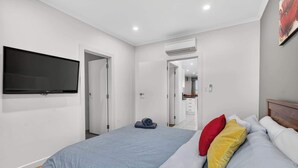 Un dormitorio con cama, televisor montado en la pared y baño a la vista a través de una puerta abierta.