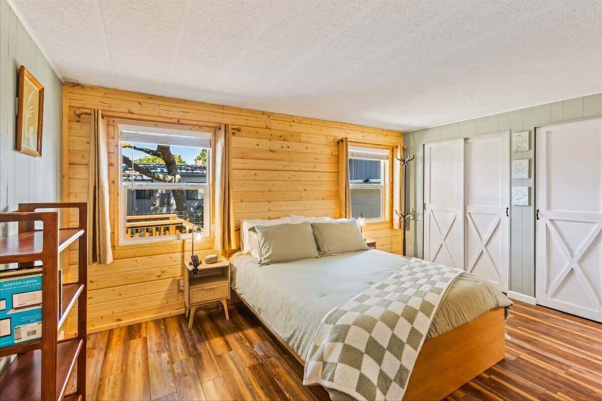 Una habitación con paneles de madera, una cama, una mesita de noche, una ventana y un armario.