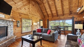 A cozy cabin interior with a stone fireplace, wooden walls, a sofa, and a dining area. - Isaiah's Cabin by Avantstay Private Hot Tub + Fire Pit + Mountain Views Near Smokies + Townsend (Townsend)