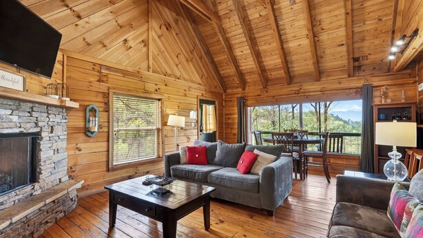 A cozy cabin interior with a stone fireplace, wooden walls, a sofa, and a dining area. - Isaiah's Cabin by Avantstay Private Hot Tub + Fire Pit + Mountain Views Near Smokies + Townsend (Townsend)
