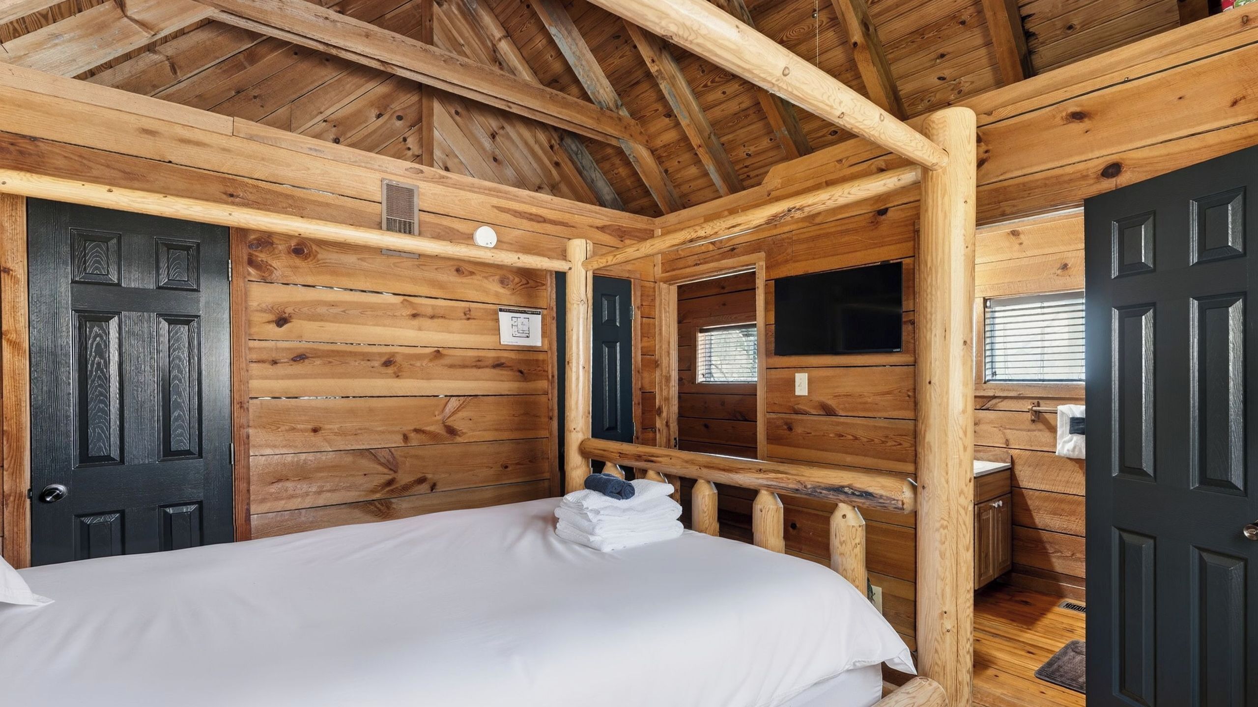 A wooden cabin room with a bed, a window, a mirror, and a door.