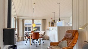 Una sala de estar acogedora con un sillón de cuero, una mesa de comedor con sillas, lámparas colgantes y una zona de cocina con una bandera.