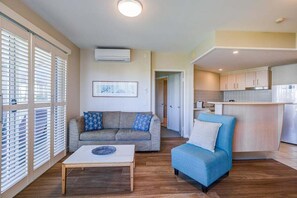Ein Wohnzimmer mit einer Couch, einem blauen Sessel, einem Couchtisch und einer Küchenzeile mit Schränken und einem Kühlschrank.