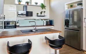 A modern kitchen with a built-in oven, stainless steel refrigerator, and a bar area with two black bar stools. - Lovely home in Hemmet with sauna (Hemmet)