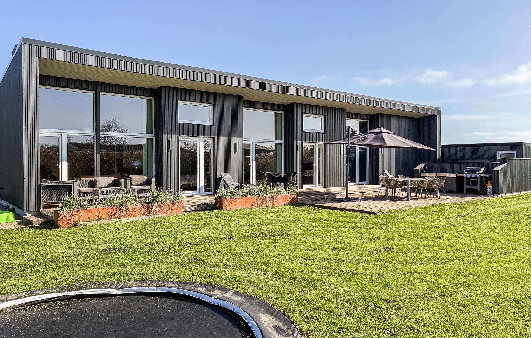 Een modern huis met twee verdiepingen, grote ramen, een terras met tuinmeubels en een barbecueplek.